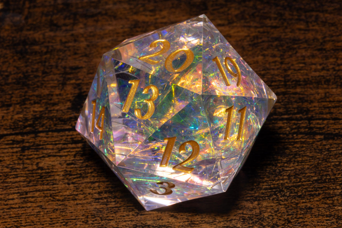 A clear, transparent crystal dice with gold numbers and markings on a wooden surface.