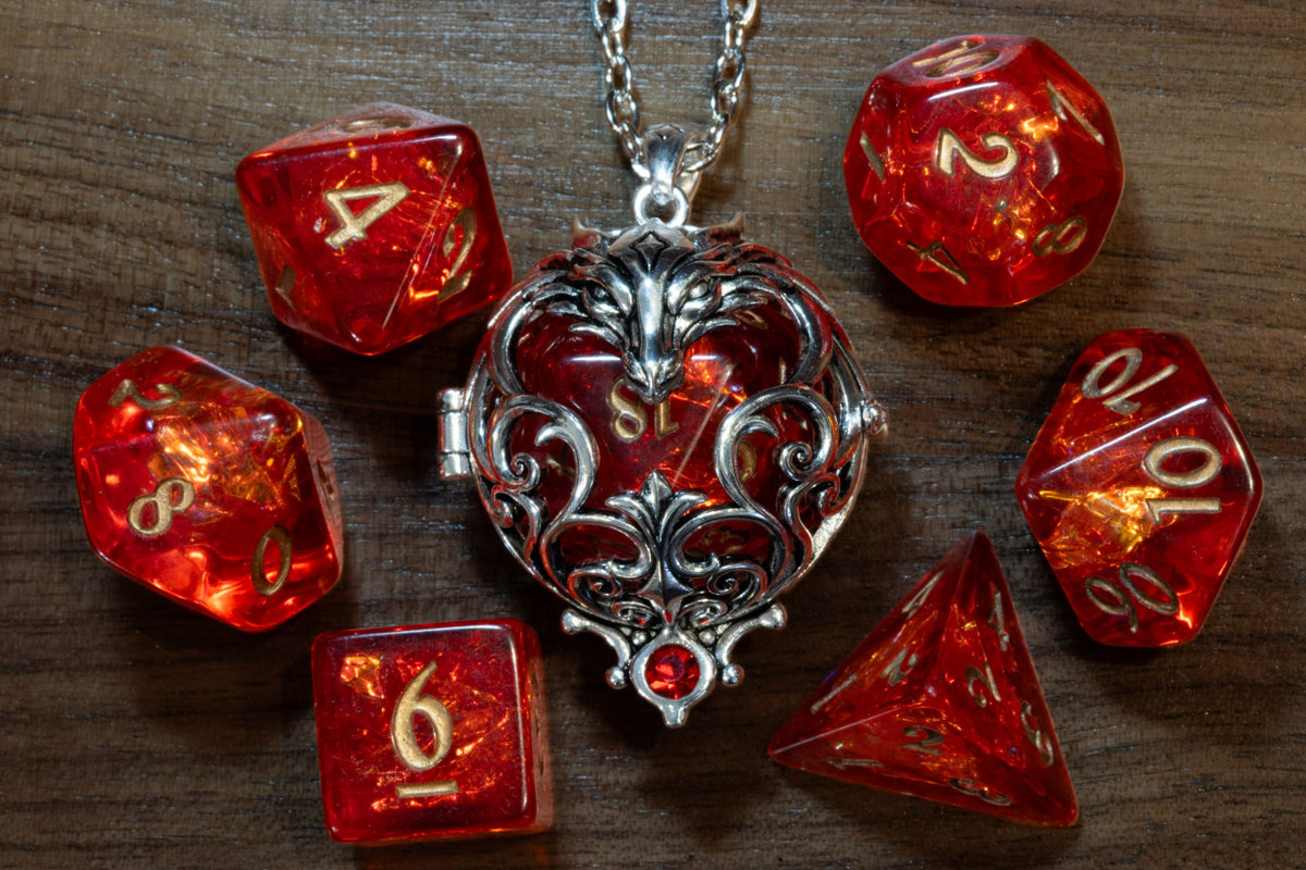 Dragon pendant in a silver finish holding a red D20, surrounded by a 7-piece red holographic dice set on wood