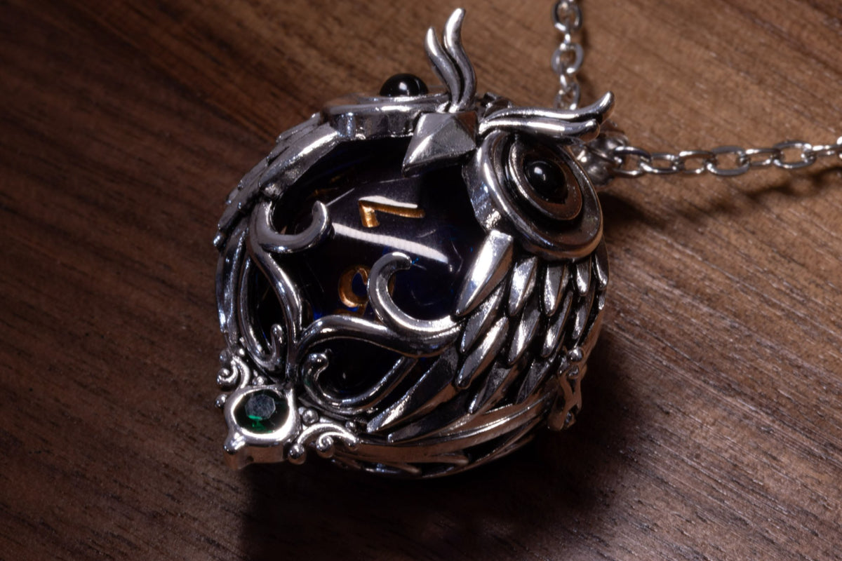 Owl pendant in a silver finish seen from the side, holding a dark blue D20, on a silver-finish chain