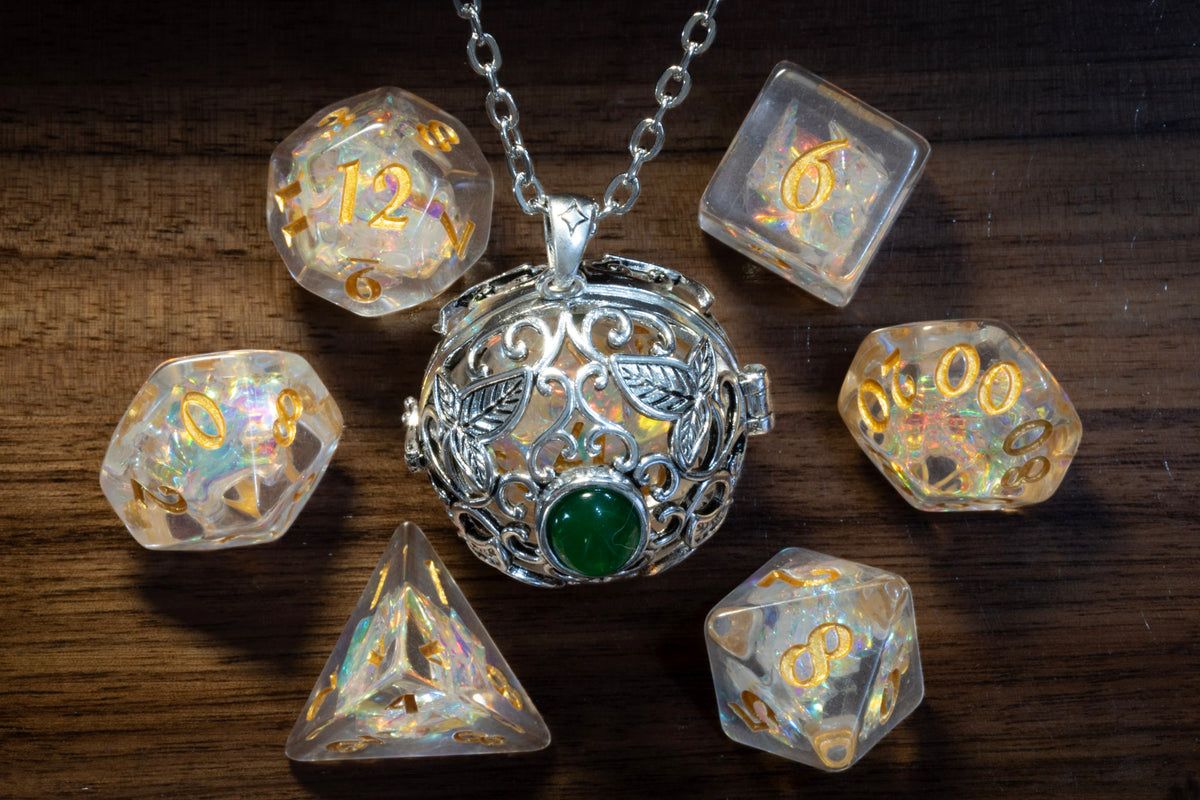 Elvish leaves pendant in a silver finish with a green cabochon, holding a Sacred Opal D20, beside the Sacred Opal dice set on wood