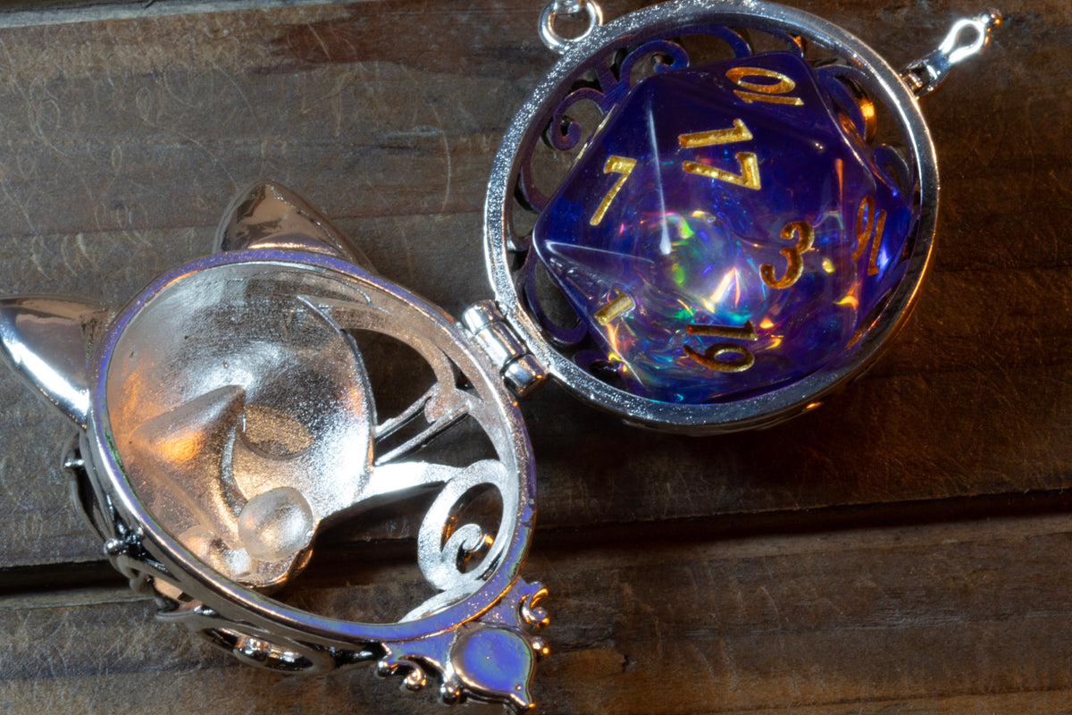Cat pendant in a silver finish shown open on its hinge, a purple holographic D20 sitting inside, the cat face lid lifted