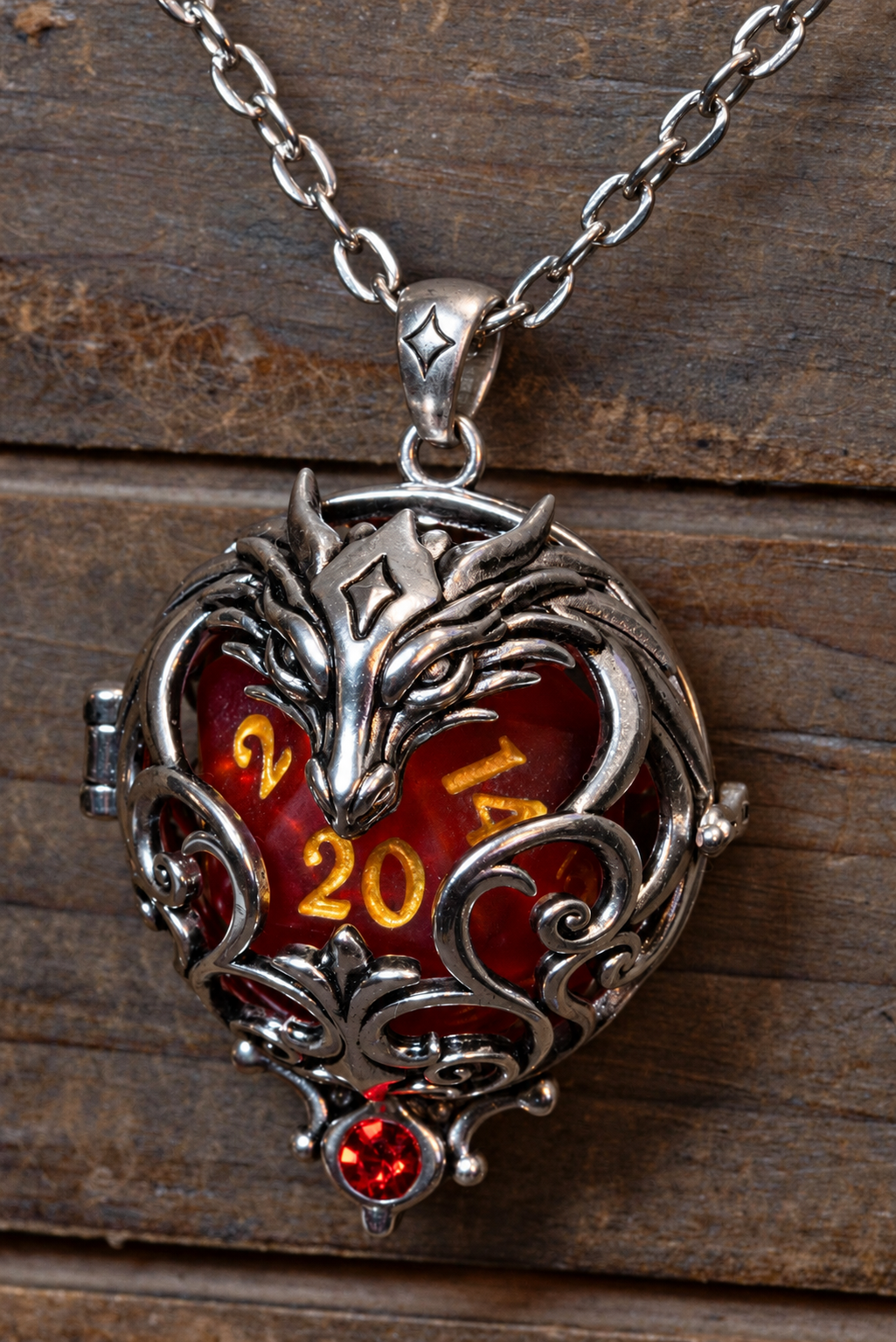 Dragon pendant in a silver finish hanging on its chain against weathered wood, red D20 inside, red crystal at the base