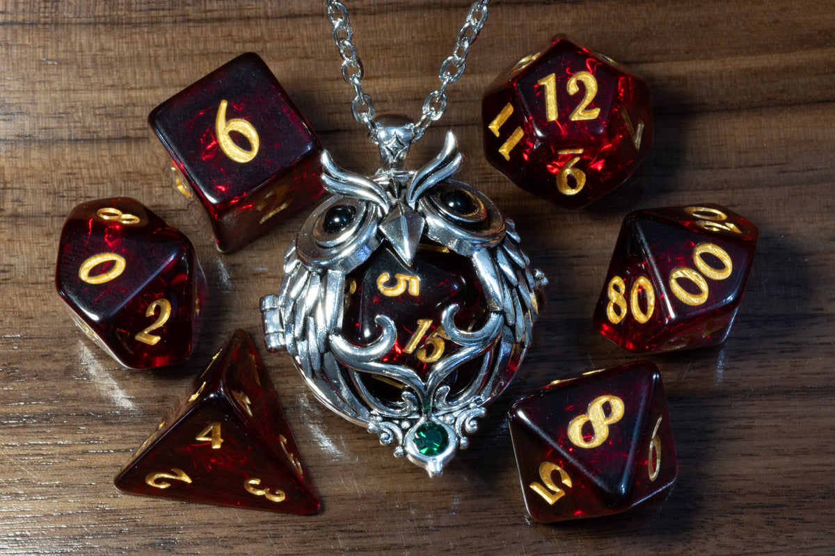 Owl pendant in a silver finish holding a Cherry Opal D20, beside the Cherry Opal dice set on wood