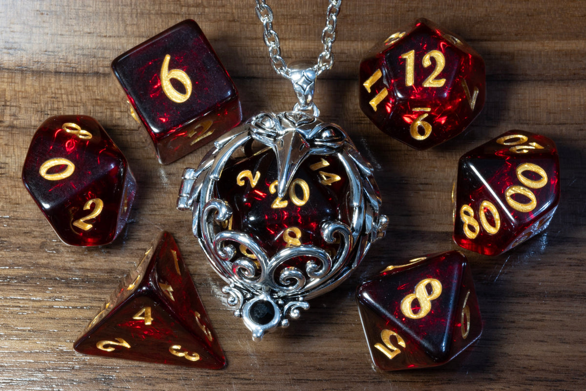 Raven pendant in a silver finish holding a Cherry Opal D20, beside the Cherry Opal dice set on wood